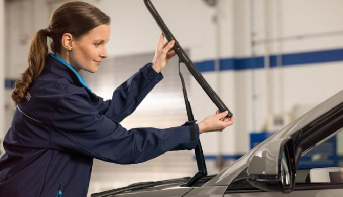 Woman inspecting a windscreen wiper on a grey car.