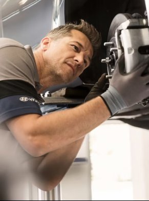 Mechanic working on a car brake system while wearing gloves and a uniform.