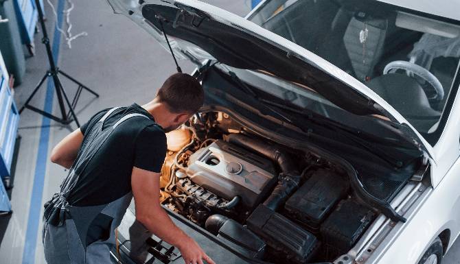 Mechanic inspecting a car engine under an open bonnet.